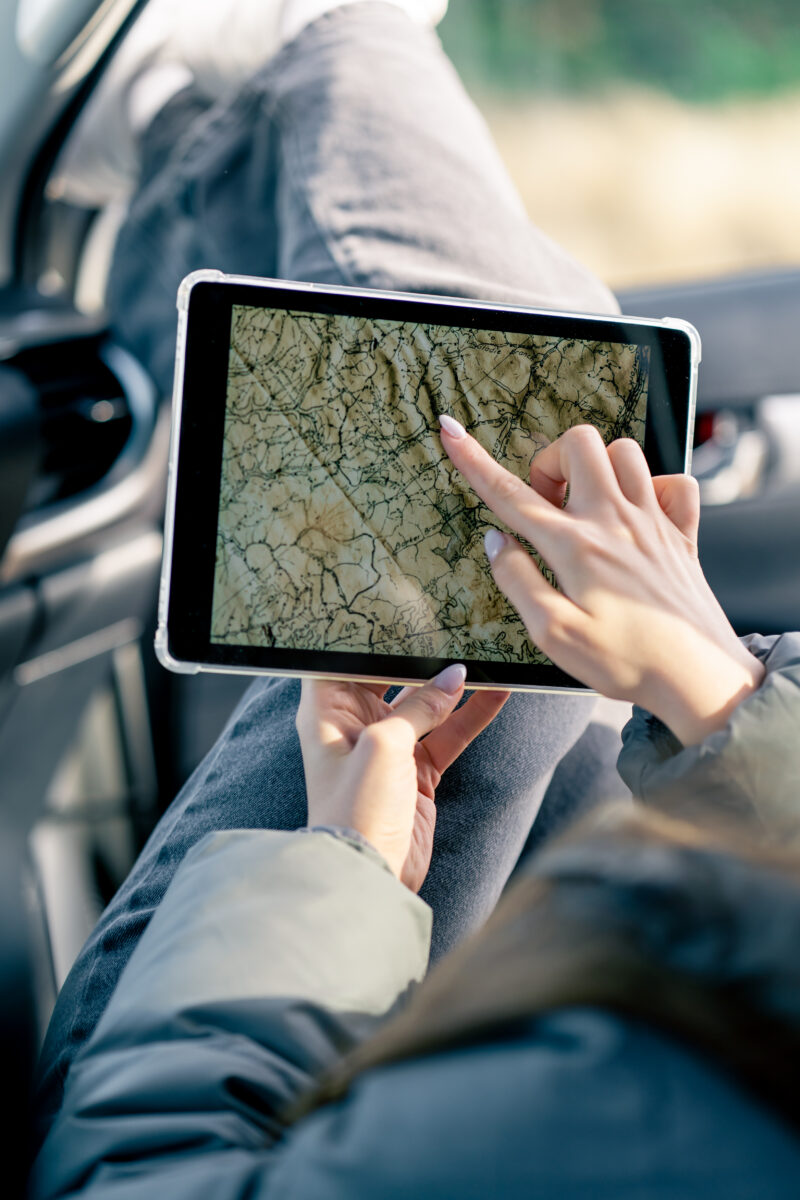Close-up shot of a tablet with a map of the area while traveling which is held by female hands in the car